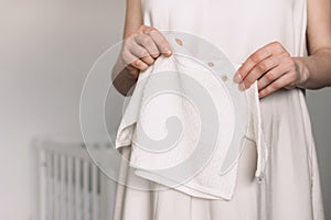 Pregnancy, maternity, preparation, baby expectation concept. Pregnant woman in white dress holding sweater, small shoes