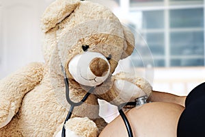 Pregnancy, medicine and healthcare concept - close up of Teddy bear playing doctor stethoscope and listens to her mother`s