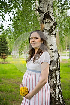 Pregnancy, motherhood, the concept of waiting-close - up of a happy pregnant woman with a big belly with a bouquet of flowers at t