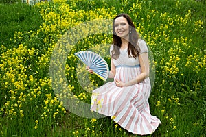 Pregnancy, motherhood, the concept of waiting-close - up of a happy pregnant woman with a big belly in a flowering meadow with a f