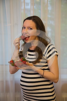 Pregnancy, motherhood, the concept of waiting-close - up of a happy pregnant woman with a big belly in a window with strawberries