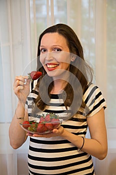 Pregnancy, motherhood, the concept of waiting-close - up of a happy pregnant woman with a big belly in a window with strawberries