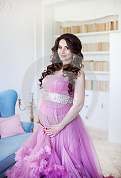 Pregnancy, motherhood and expectation concept - a pregnant woman dressed in pink evening dress smiles