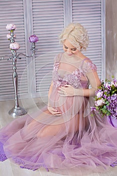 Pregnancy, motherhood and happy future mother concept - pregnant woman in airy violet dress with bouquet flowers against colorful