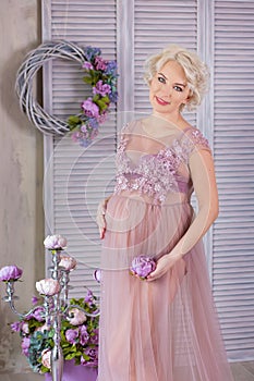 Pregnancy, motherhood and happy future mother concept - pregnant woman in airy violet dress with bouquet flowers against colorful