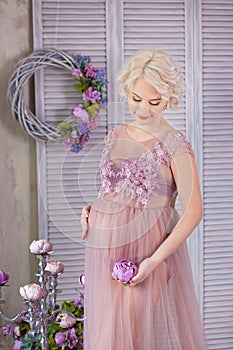 Pregnancy, motherhood and happy future mother concept - pregnant woman in airy violet dress with bouquet flowers against colorful