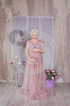 Pregnancy, motherhood and happy future mother concept - pregnant woman in airy violet dress with bouquet flowers against colorful