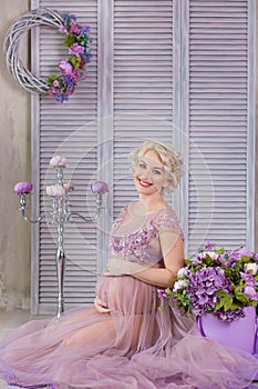 Pregnancy, motherhood and happy future mother concept - pregnant woman in airy violet dress with bouquet flowers against colorful