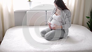pregnancy, motherhood, people, expectation concept - happy pregnant woman touching her tummy in bed at home caring