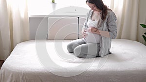 Pregnancy, motherhood, people, expectation concept - happy pregnant woman touching her tummy in bed at home caring