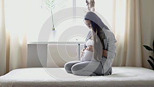 pregnancy, motherhood, people, expectation concept - happy pregnant woman touching her tummy in bed at home caring