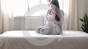 pregnancy, motherhood, people, expectation concept - happy pregnant woman touching her tummy in bed at home caring