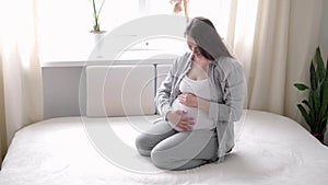 pregnancy, motherhood, people, expectation concept - happy pregnant woman touching her tummy in bed at home caring