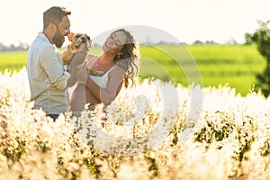 Pregnancy, motherhood, people and expectation concept, laughing couple holding dog on lap during sunset in the countryside