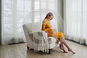 Pregnancy motherhood people expectation future. Pregnant woman with big belly sitting on chair near window at home. Girl