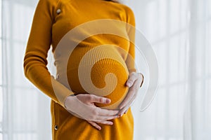 Pregnancy motherhood people expectation future. Pregnant woman hands touching big belly near window at home. Girl