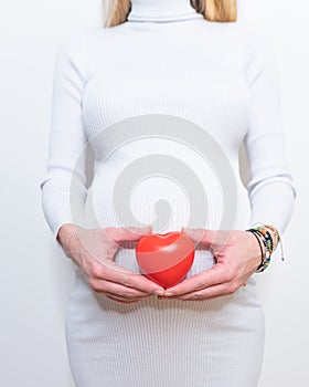 Pregnancy, motherhood, people, love and expectation concept - close up of happy pregnant woman holding heart shape on her bare