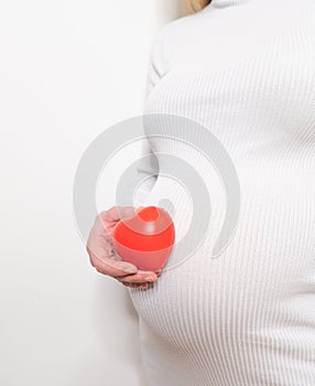 pregnancy, motherhood, people, love and expectation concept - close up of happy pregnant woman holding heart shape on her bare