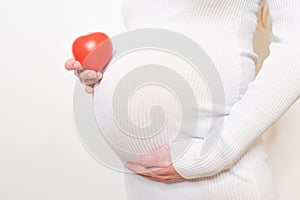 pregnancy, motherhood, people, love and expectation concept - close up of happy pregnant woman holding heart shape on her bare