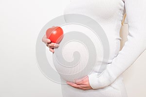 pregnancy, motherhood, people, love and expectation concept - close up of happy pregnant woman holding heart shape on her bare