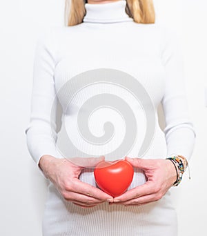 Pregnancy, motherhood, people, love and expectation concept - close up of happy pregnant woman holding heart shape on her bare