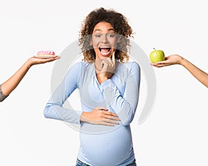 Pregnancy nutrition. Emotional pregnant woman choosing between apple and donut