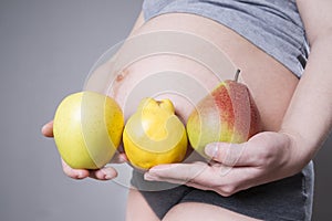 Pregnancy and nutrition - pregnant woman with fruits in hand on gray background