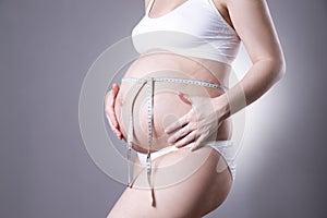 Pregnancy and nutrition - pregnant woman with measuring tape on gray background