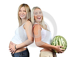 Pregnancy. One woman is holding pregnant belly, other woman is holding watermelon. Isolated. Two happy girls laughing.