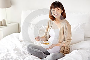 Happy pregnant woman eating cereal flakes at home