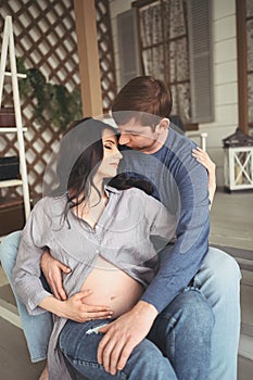 Pregnancy and people concept - happy man hugging his beautiful pregnant wife at home. Future parents waiting unborn baby.