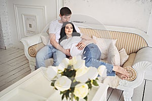 Pregnancy and people concept - happy man hugging his beautiful pregnant wife at home. Future parents waiting unborn baby.