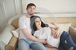 Pregnancy and people concept - happy man hugging his beautiful pregnant wife at home. Future parents waiting unborn baby.