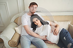 Pregnancy and people concept - happy man hugging his beautiful pregnant wife at home. Future parents waiting unborn baby.