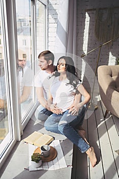 Pregnancy and people concept - happy man hugging his beautiful pregnant wife at home. Future parents waiting unborn baby.