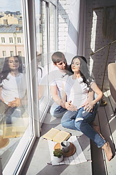 Pregnancy and people concept - happy man hugging his beautiful pregnant wife at home. Future parents waiting unborn baby.