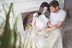 Pregnancy and people concept - happy man hugging his beautiful pregnant wife at home. Future parents waiting unborn baby.