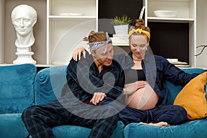 pregnancy and people concept - happy man hugging his pregnant wife sitting at home on the couch.