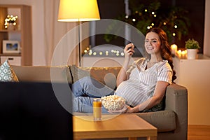 Pregnant woman with popcorn watching tv at home