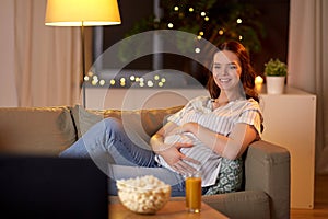 Happy smiling pregnant woman watching tv at home