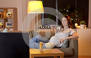 Pregnant woman with remote control watching tv