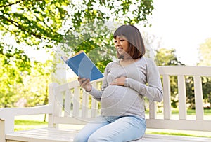 Happy pregnant asian woman reading book at park