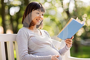 Happy pregnant asian woman reading book at park