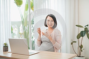 pregnancy  people and rest concept - close up of happy pregnant woman eating yogurt for breakfast at home