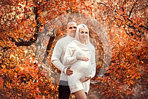 Pregnancy. Pregnant couple in white outfits enjoying in autumn forest park. Beautiful blond woman with husband. Parenthood