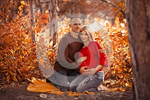 Pregnancy. Pregnant couple in white outfits enjoying in autumn forest park. Loving man hugging his beautiful wife. Parenthood