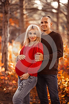 Pregnancy. Pregnant couple in white outfits enjoying in autumn forest park. Loving man hugging his beautiful wife. Parenthood