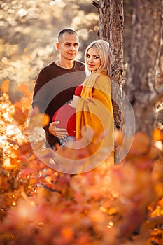 Pregnancy. Pregnant couple in white outfits enjoying in autumn forest park. Loving man hugging his beautiful wife. Parenthood