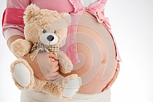 Pregnancy. Pregnant woman holding teddy bear toy in his hand, st