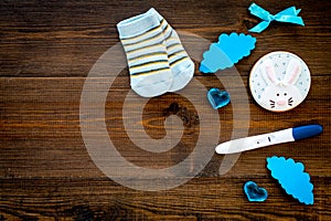 Pregnancy and preparation for childbirth. Babyshower. Pregnancy test near socks and hearts wooden background top view